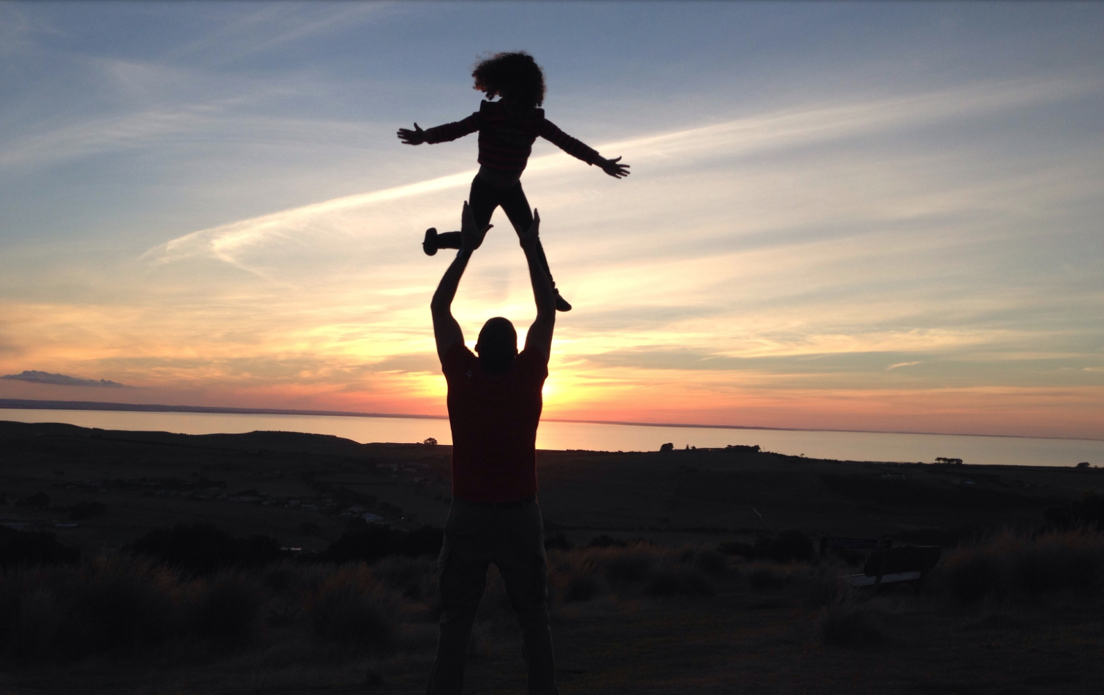 Silhouette of a man holding a child in the air at sunset