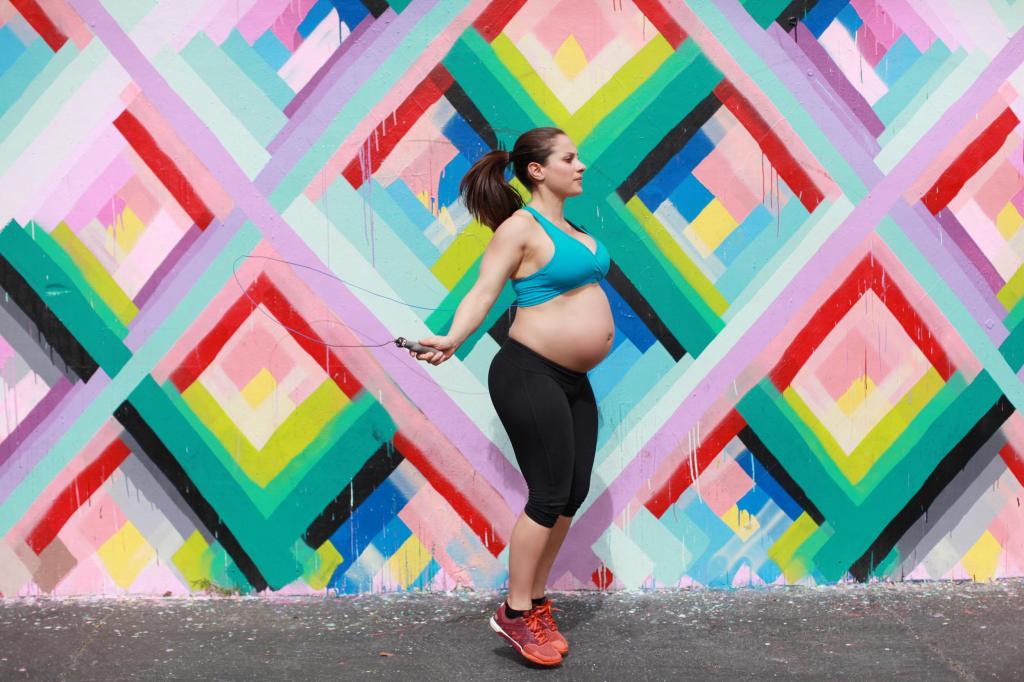 A pregnant athlete performs jump rope repetitions in front of a colorful wall