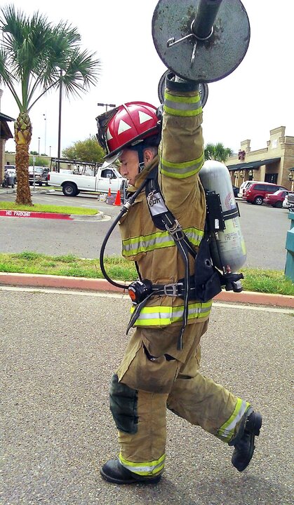 Firefighter in gear holding a barbell overhead